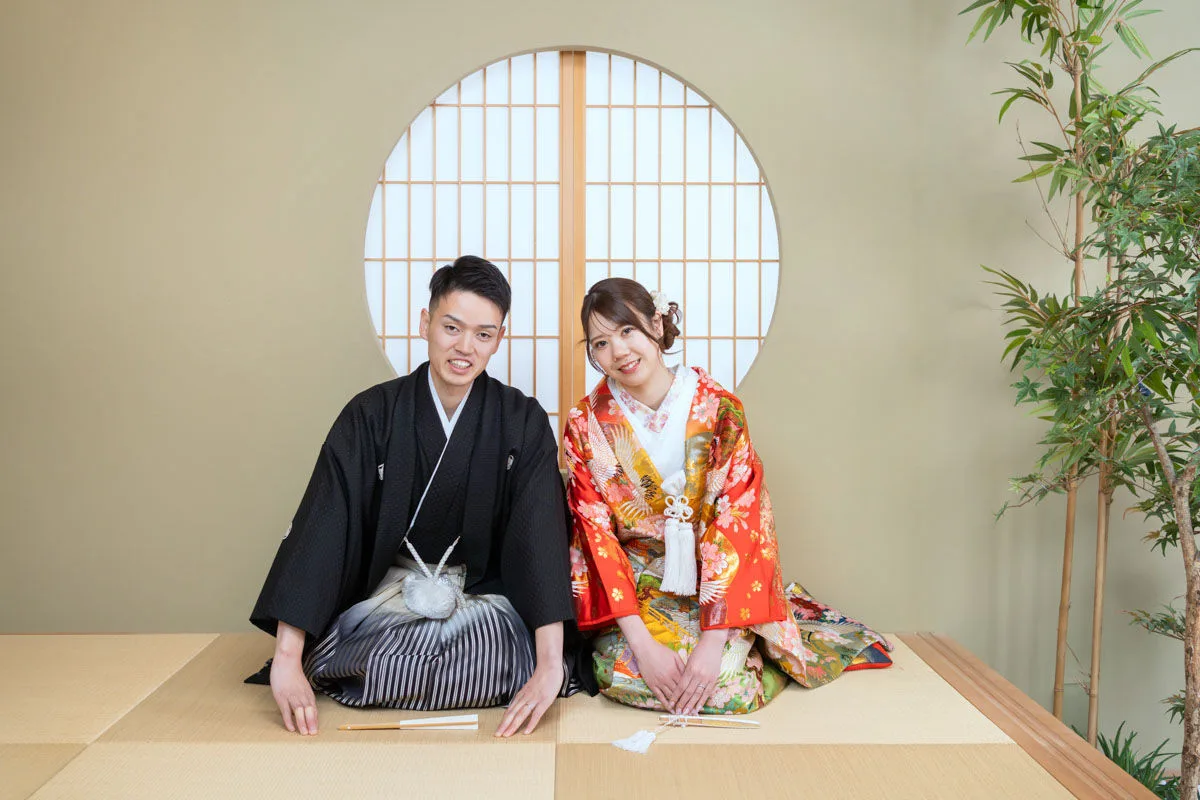 和装を着て、和室の丸窓の前で正座している新郎新婦の結婚写真