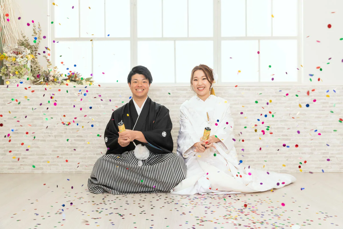 白無垢と紋付袴で並んで座り、クラッカーの紙吹雪に包まれる新郎新婦のスタジオ前撮り