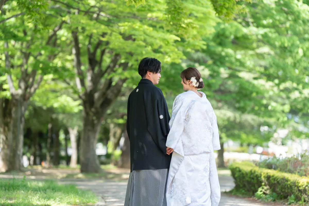 新緑の中の白無垢姿と黒色の紋付袴の新郎新婦