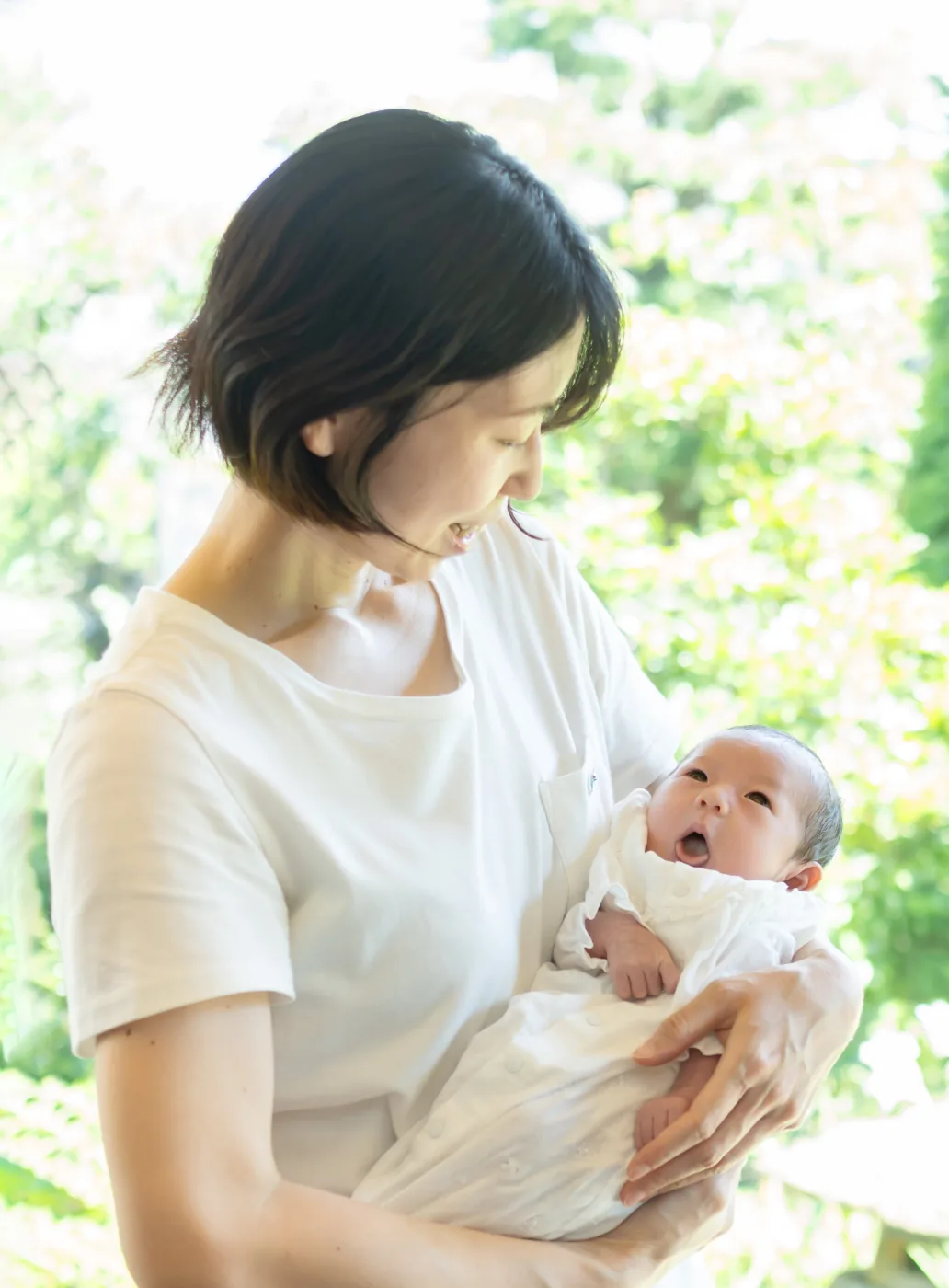 庭の見える窓辺で、あくびをする生後1か月ごろの赤ちゃんを抱く母親